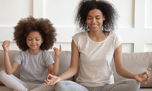 Mother and daughter meditating while sitting on a couch