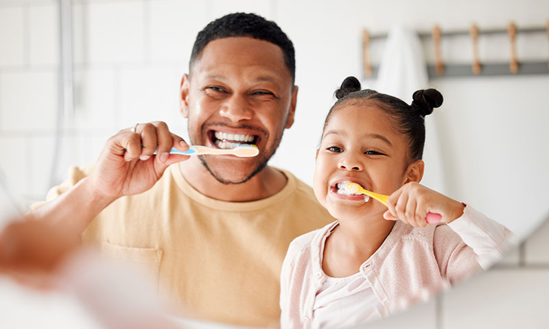 Little girl and dad brushing their teeth.