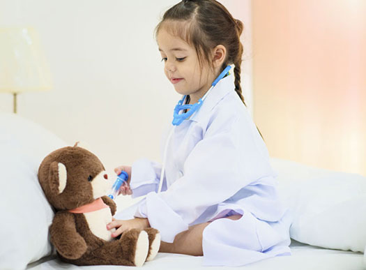 Little girl playing doctor on a teddy bear.